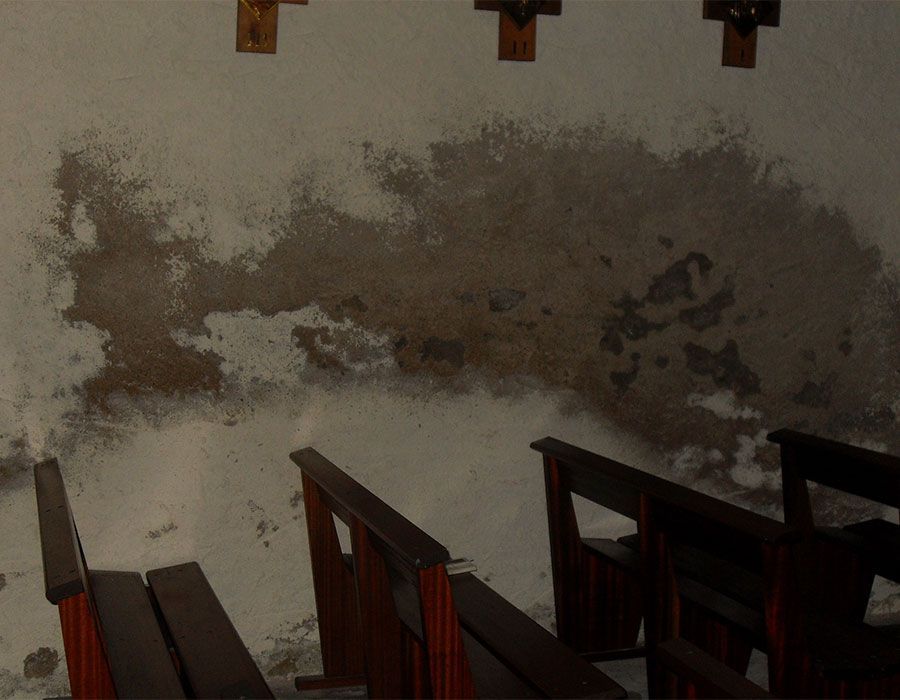 Mur en plâtre endommagé au-dessus de bancs en bois à l'intérieur d'une église sombre.