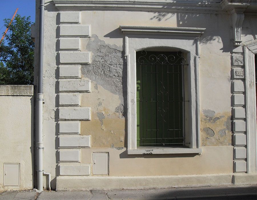 Façade d'immeuble blanche délabrée avec une fenêtre à barreaux verts et de la peinture écaillée.