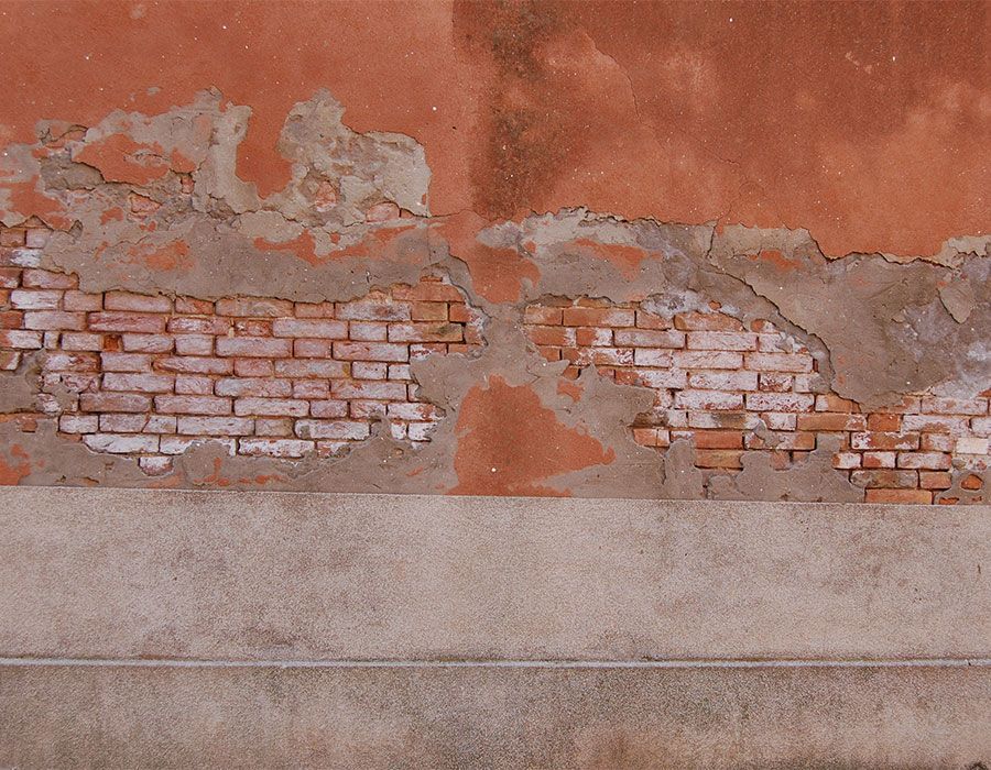 Mur orange délavé, au plâtre écaillé laissant apparaître la brique et une plinthe grise.