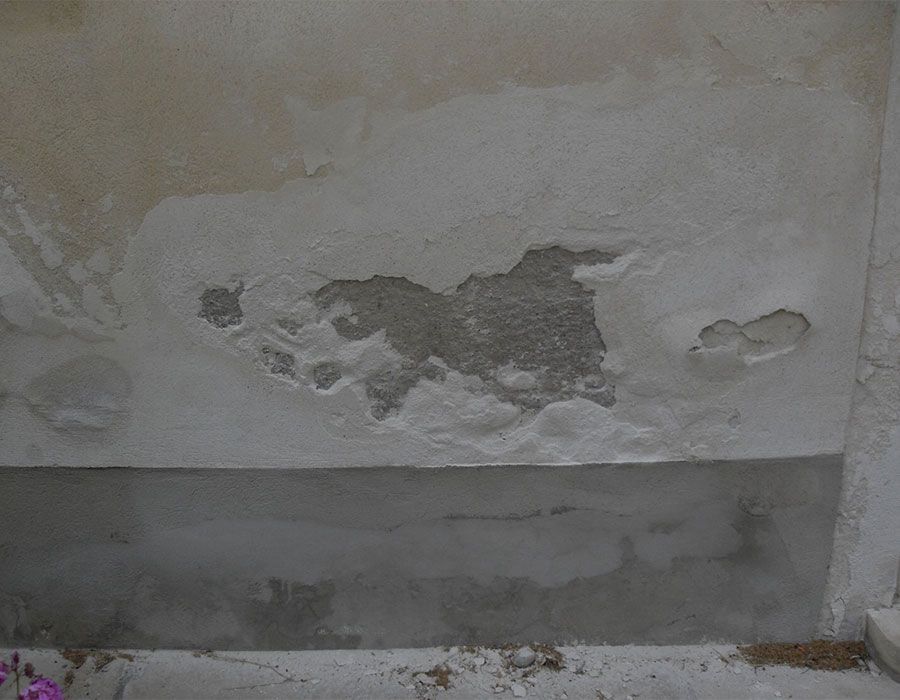 Mur extérieur endommagé, peinture écaillée et plâtre gris rapiécé près de la base