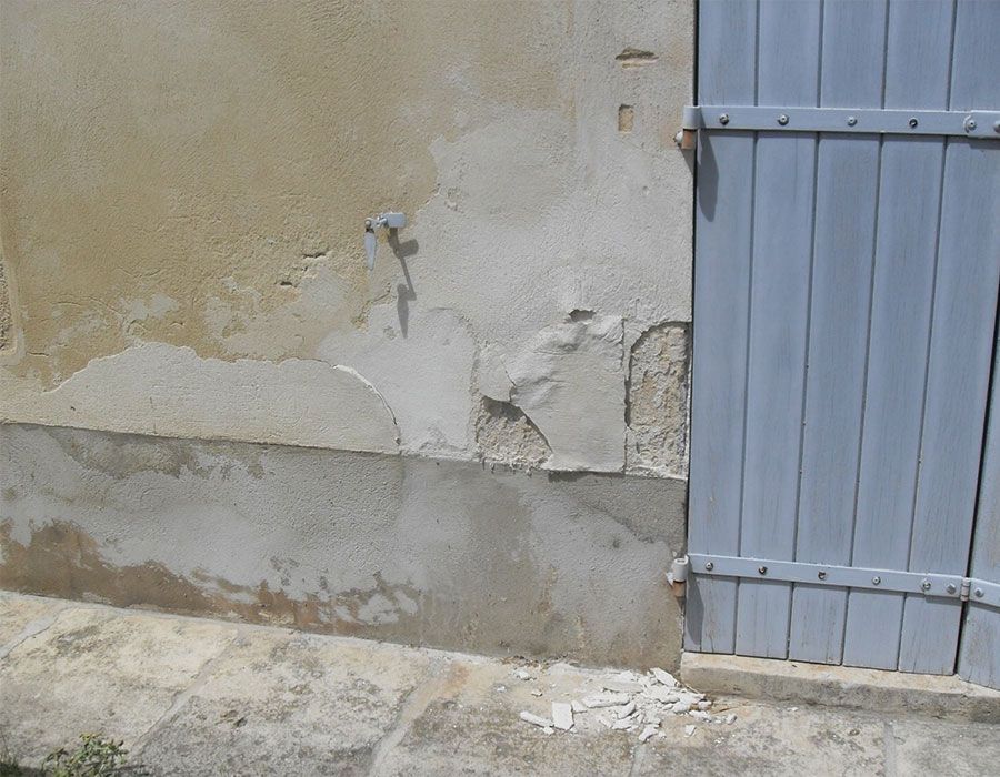 Mur en stuc fissuré à côté d'une porte métallique grise dont la peinture s'écaille