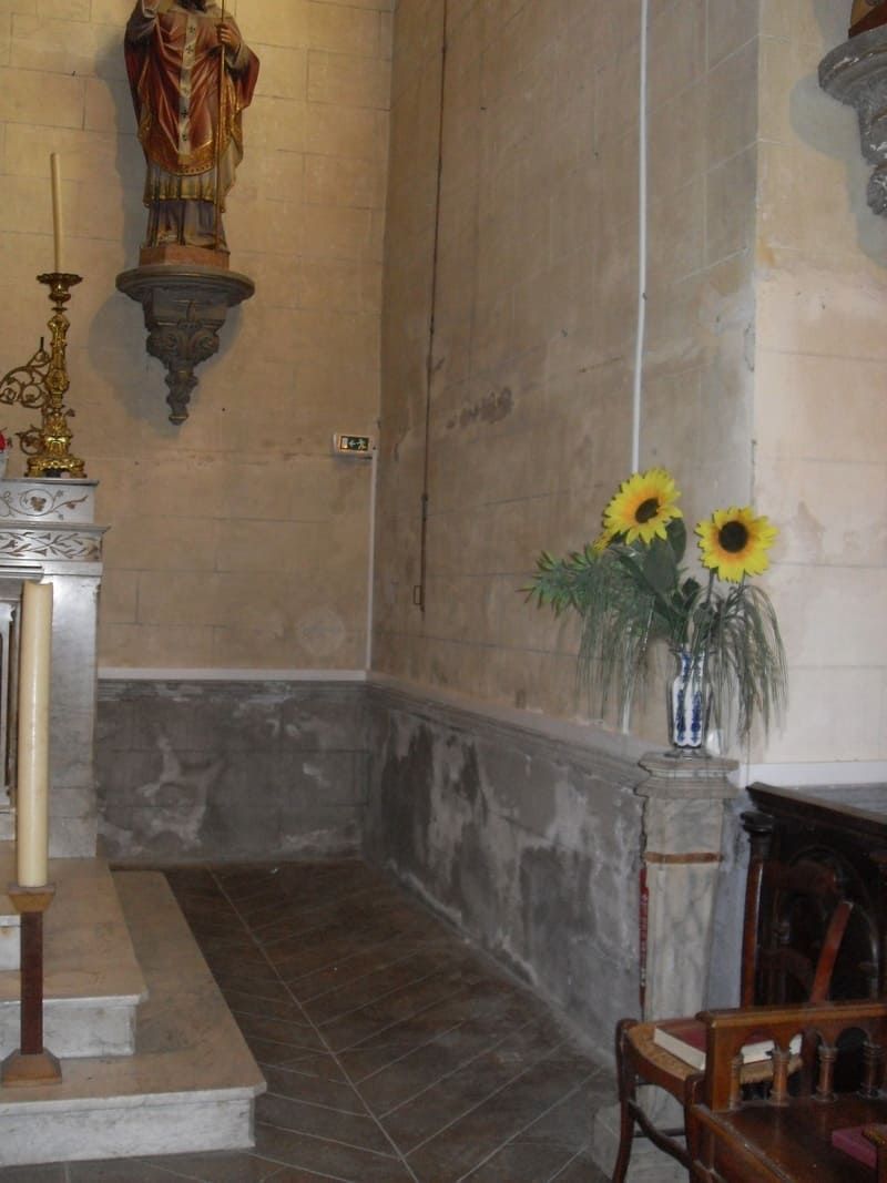 Alcôve d'église avec une statue, un autel et un vase de tournesols à côté d'un mur de pierre.