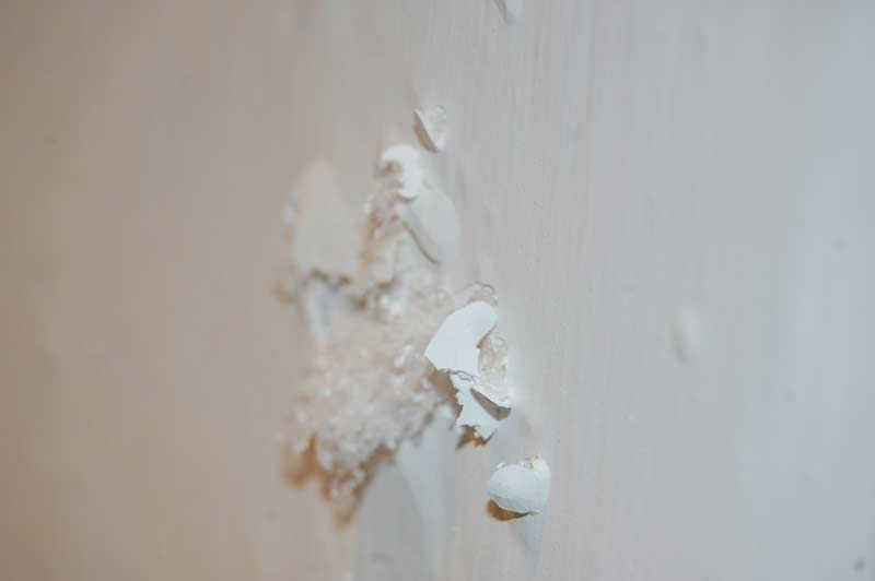 Peinture blanche écaillée sur un mur, laissant apparaître du plâtre écaillé en dessous.