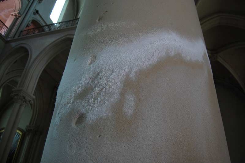 Un grand pilier de pierre à l'intérieur d'une cathédrale, avec une tache blanche de mousse ou de résidu à sa surface.