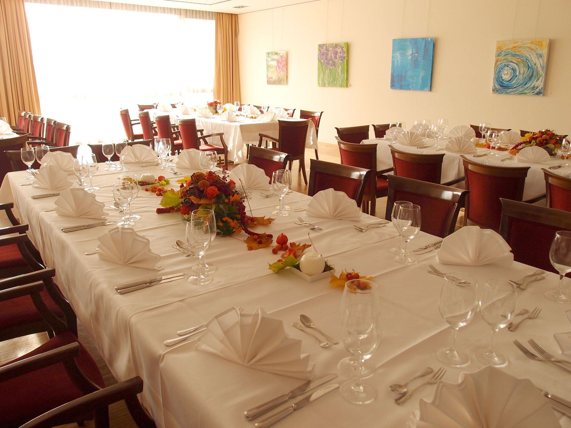 Ein langer Tisch in einem Restaurant mit Blumen darauf. Der Tisch ist gedeckt.