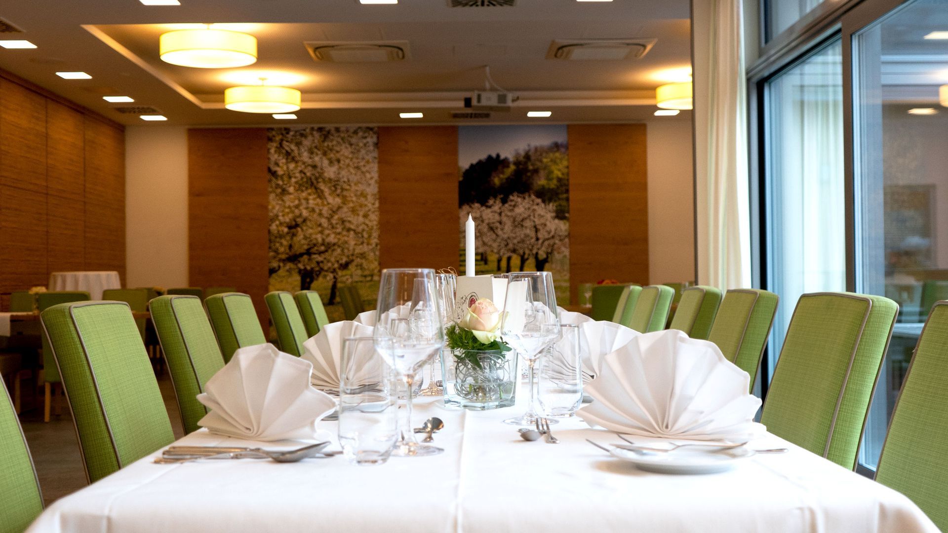 Ein langer Tisch mit einer weißen Tischdecke und grünen Stühlen in einem Restaurant.