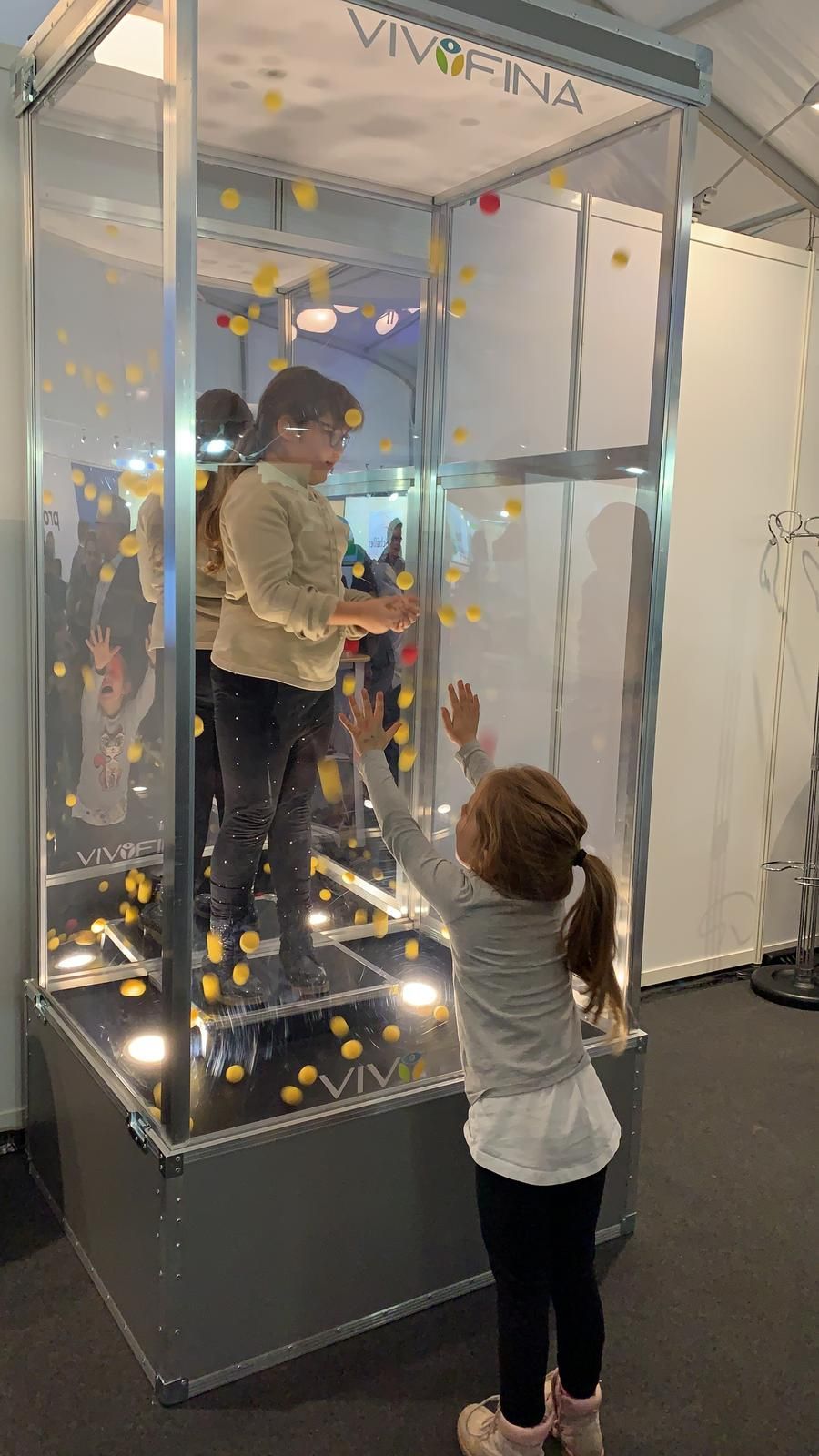 Drei Ansichten einer Glasvitrine mit einer Person darin. Schwarzer Sockel, Beleuchtung und ausgestellte Gegenstände.