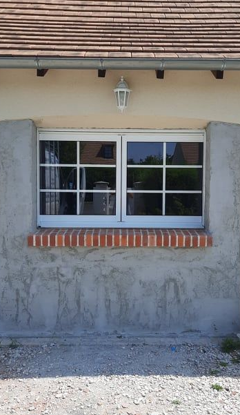 Fenêtre à cadre blanc sur le mur d'une maison en stuc, sous un toit de tuiles.