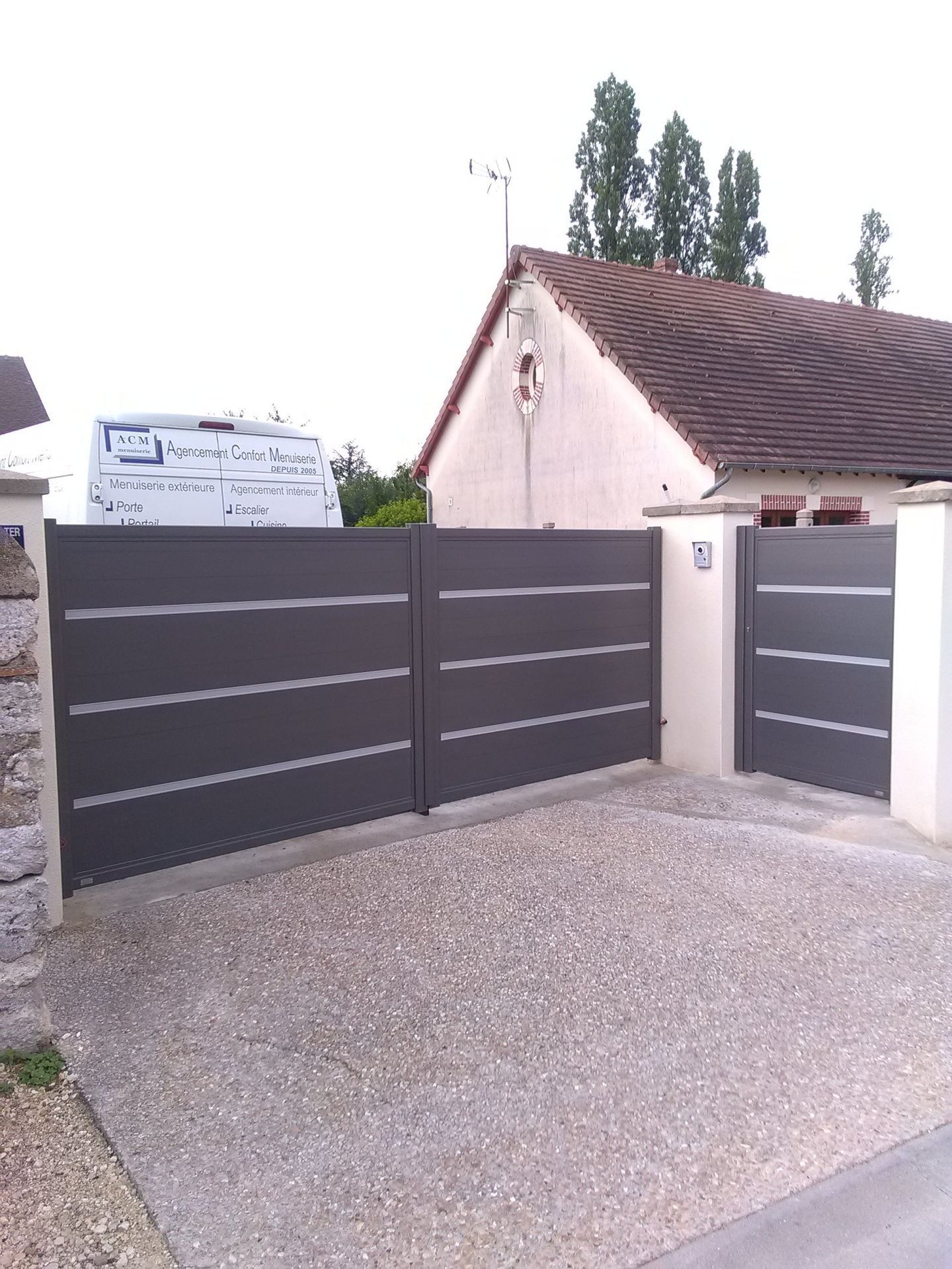Portail coulissant et portillon piéton gris foncé moderne à l'entrée d'une allée de maison.