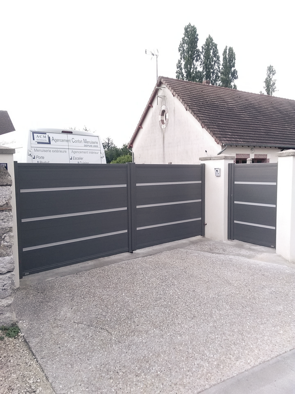 Portail moderne gris foncé avec piliers blancs à l'entrée d'une allée résidentielle.