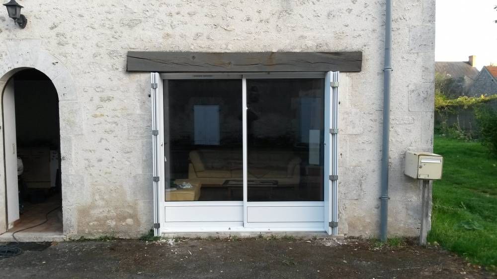 Façade en pierre d'une maison avec une grande fenêtre et un auvent en bois.