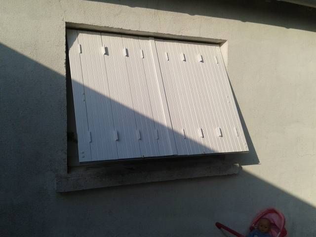 Volets en métal blanc sur un mur beige.