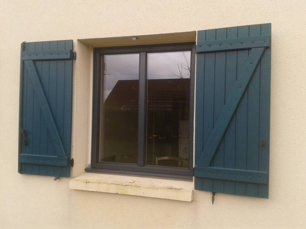 Fenêtre à volets bleus sur un mur beige.