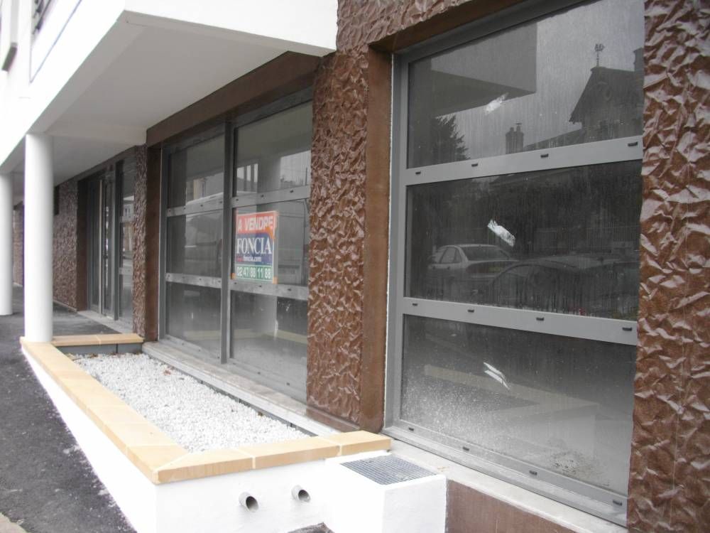 Vitrines de local, allée de gravier et jardinière en béton le long de la façade