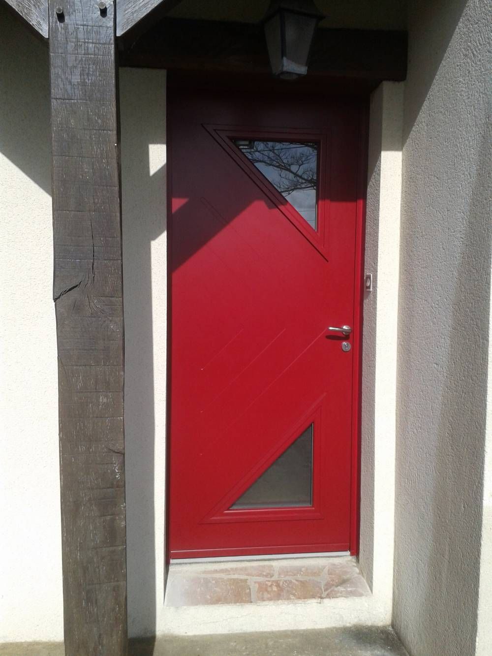 Porte d'entrée rouge avec fenêtres triangulaires dans une entrée en retrait.