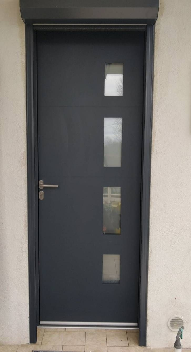 Porte d'entrée gris foncé avec d'étroites fenêtres verticales et une poignée argentée sur un mur clair.