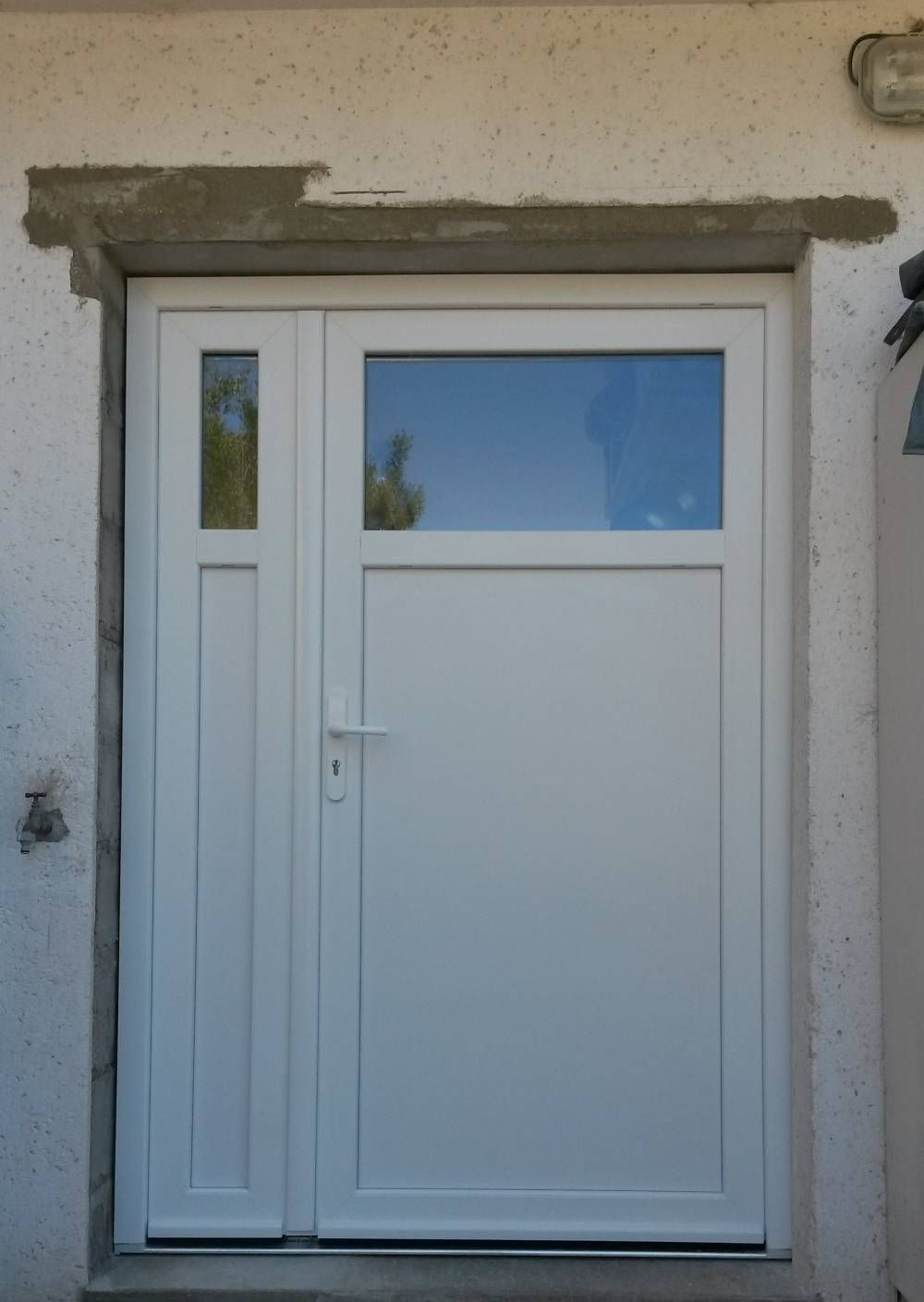 Porte d'entrée blanche avec fenêtre latérale étroite et panneau de verre dépoli dans un mur en stuc