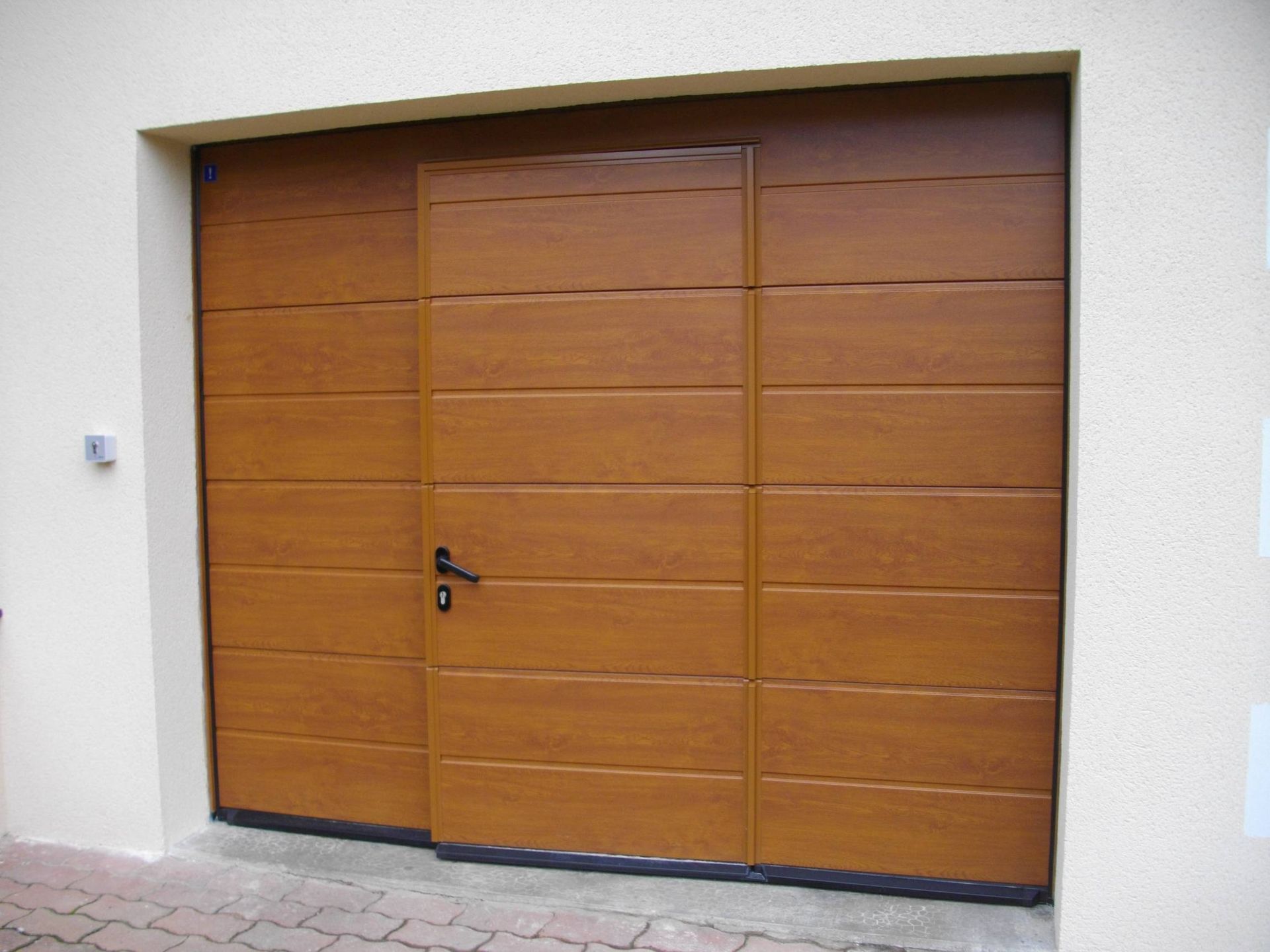 Porte de garage double en bois avec poignée noire encastrée dans un mur blanc.