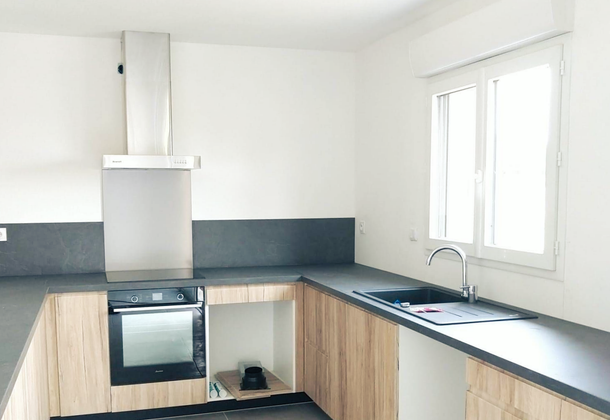 Cuisine moderne et lumineuse avec murs blancs, placards en bois, plans de travail foncés.
