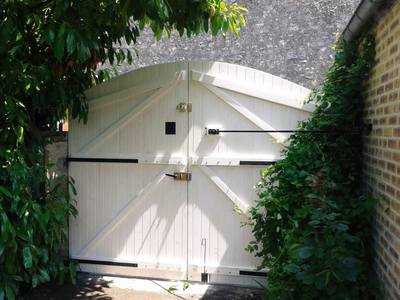 Abri de jardin en bois blanc à double porte, encadré par un dense feuillage vert et lierre.