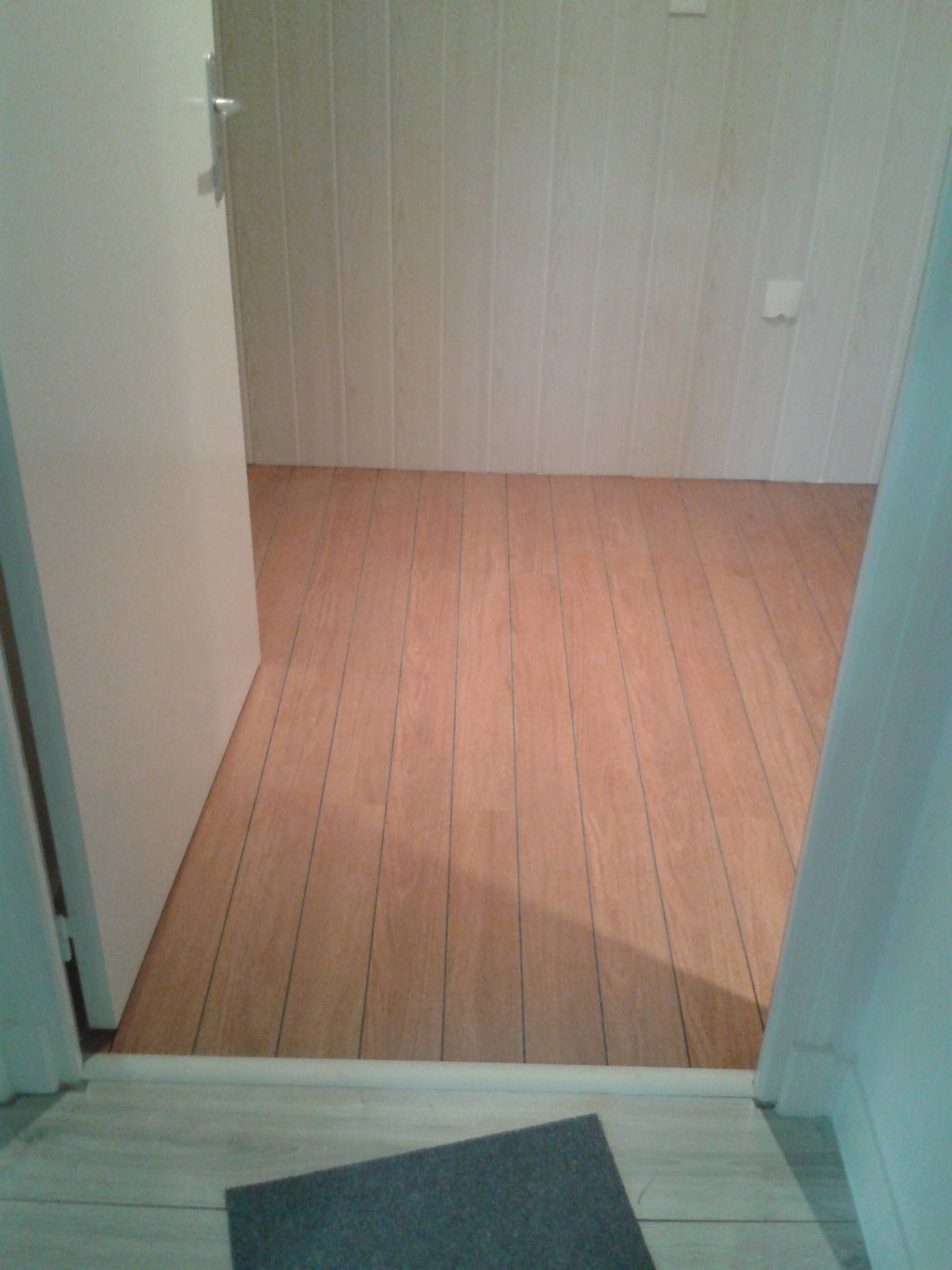 Pièce vide avec parquet clair et murs blancs, vue à travers une porte.