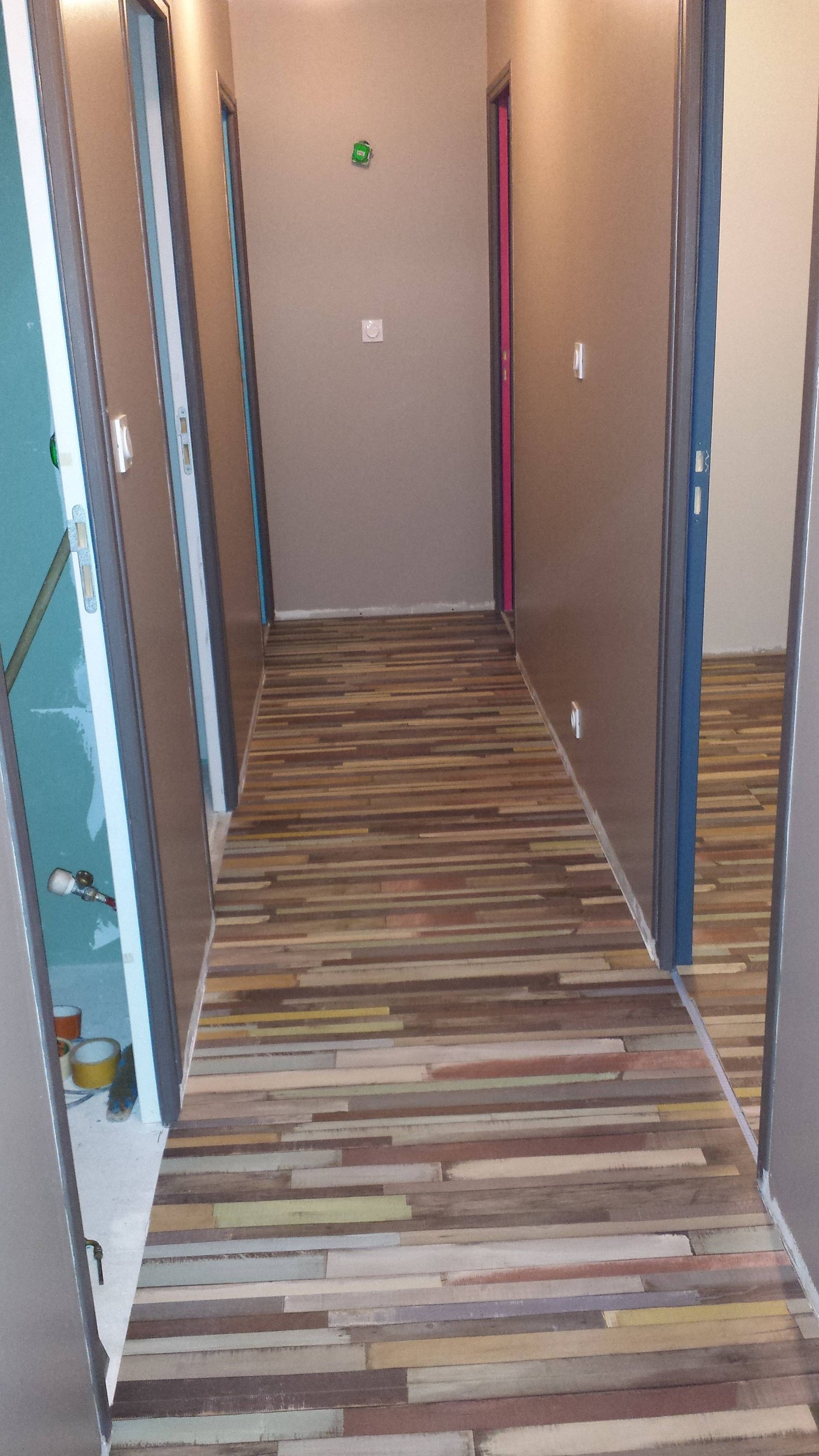 Couloir étroit avec moquette à rayures multicolores et murs beiges menant à une porte fermée.