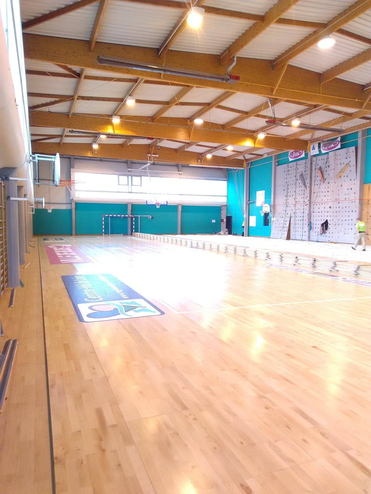 Gymnase vide avec parquet, murs turquoise et éclairage zénithal vif.