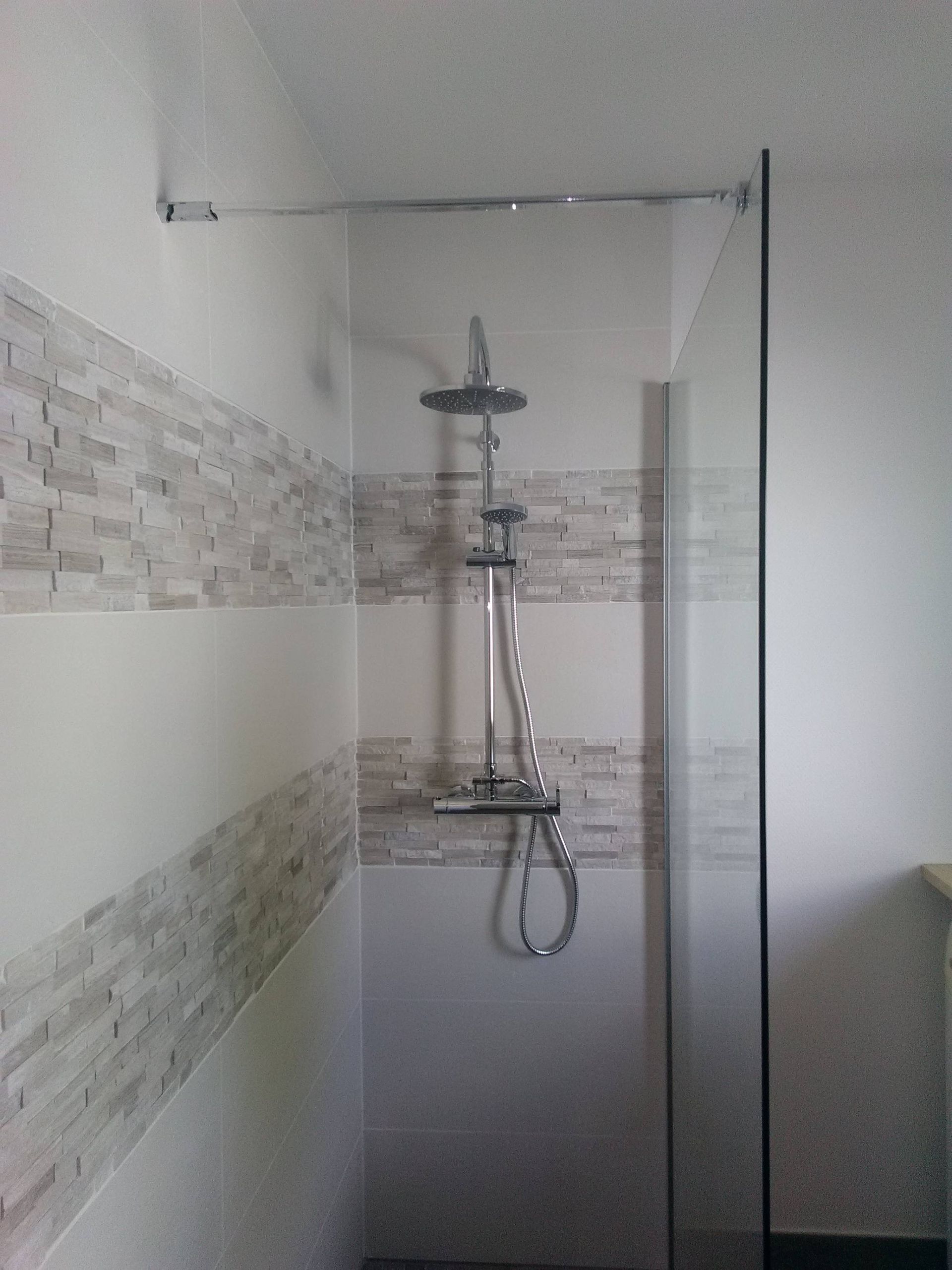 Cabine de douche moderne avec porte en verre, murs carrelés et pommeau de douche mural.