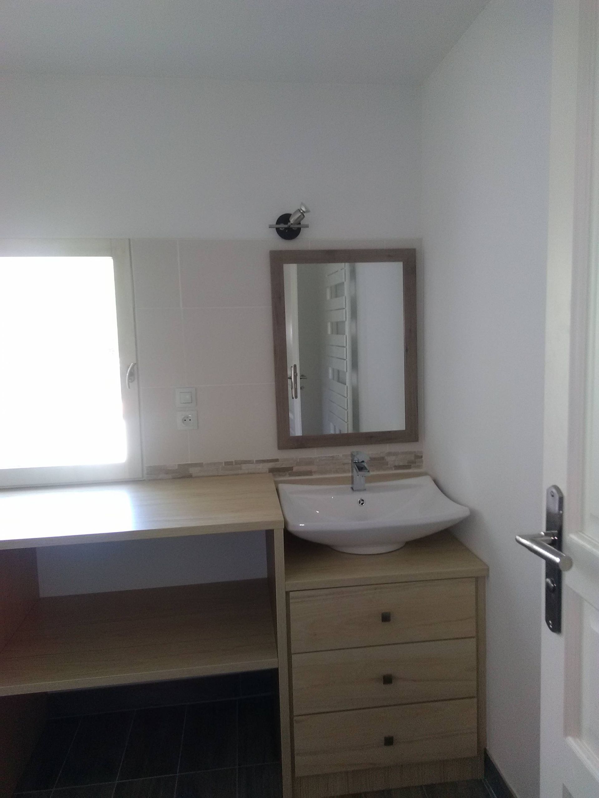 Petite salle de bains avec lavabo, miroir, meuble-lavabo en bois et lumière naturelle abondante.