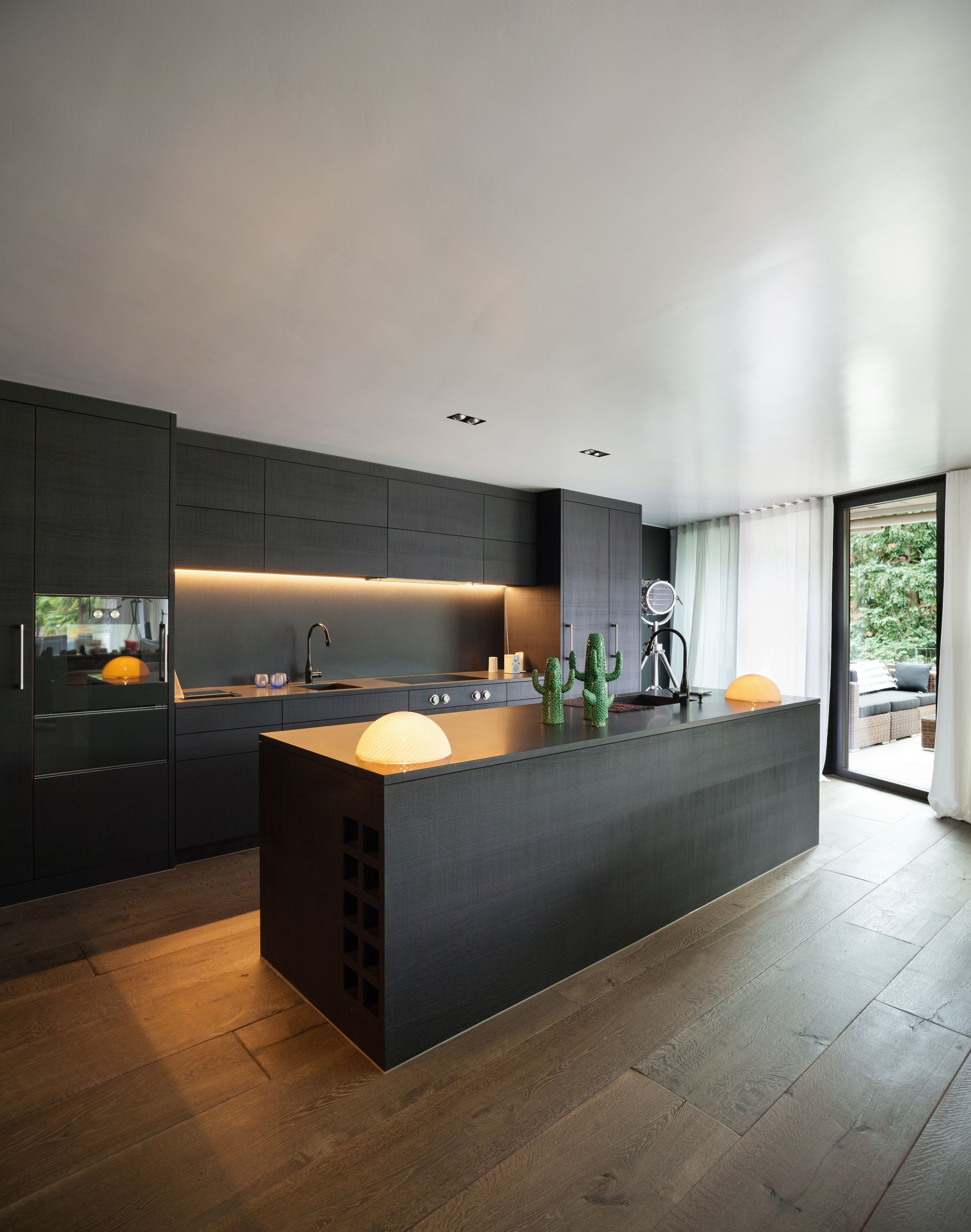 Cuisine moderne noire avec îlot central, éclairage sous les meubles hauts.