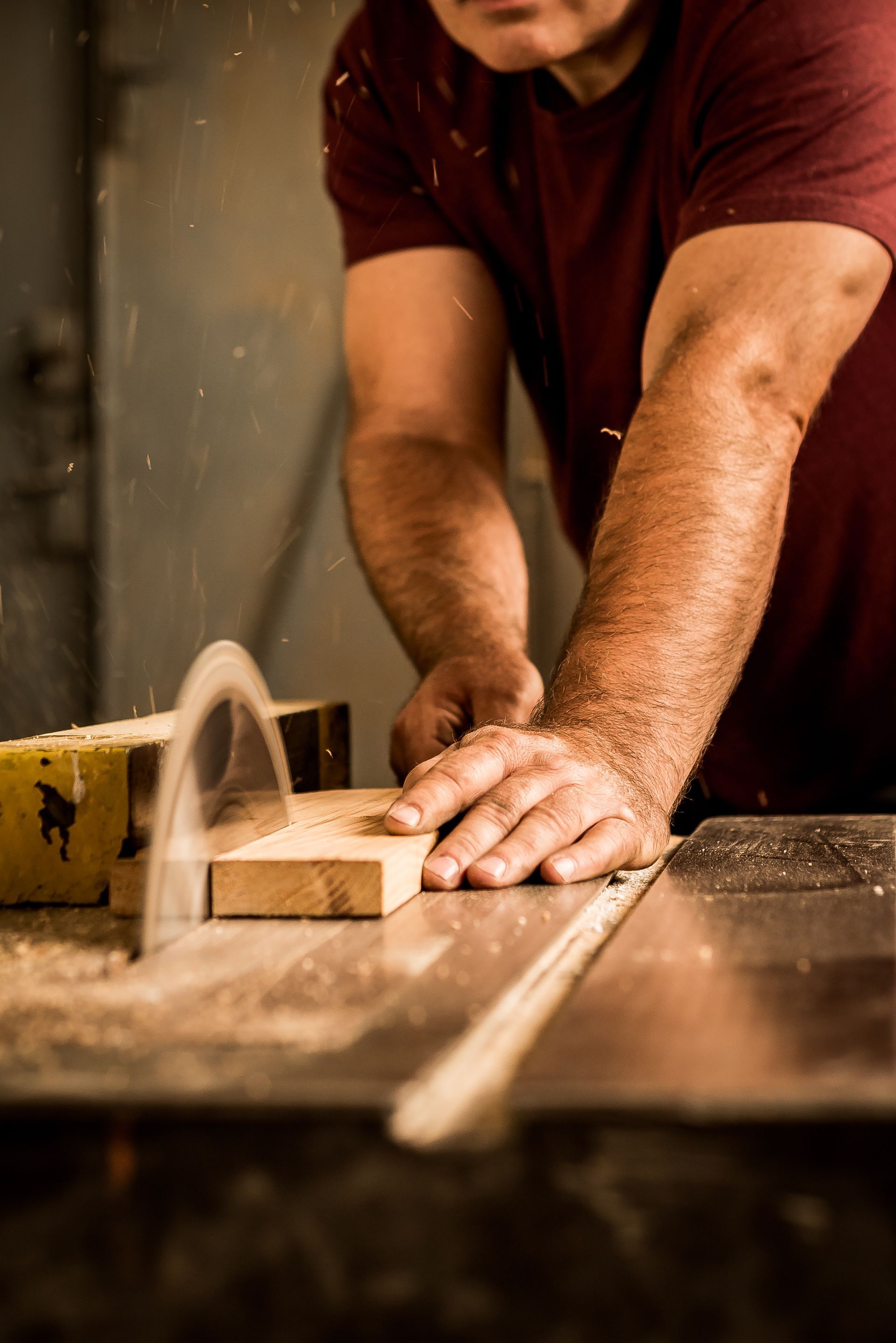 Une personne coupe une planche de bois sur une scie circulaire dans un atelier, projetant de la sciure de bois.