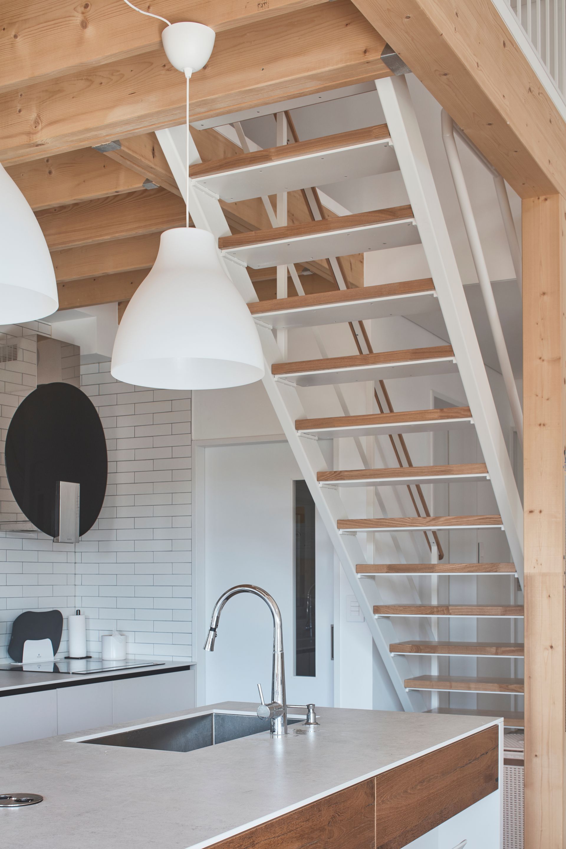 Cuisine moderne avec suspensions blanches, plafond en bois et escalier ouvert au-dessus de l'îlot central.