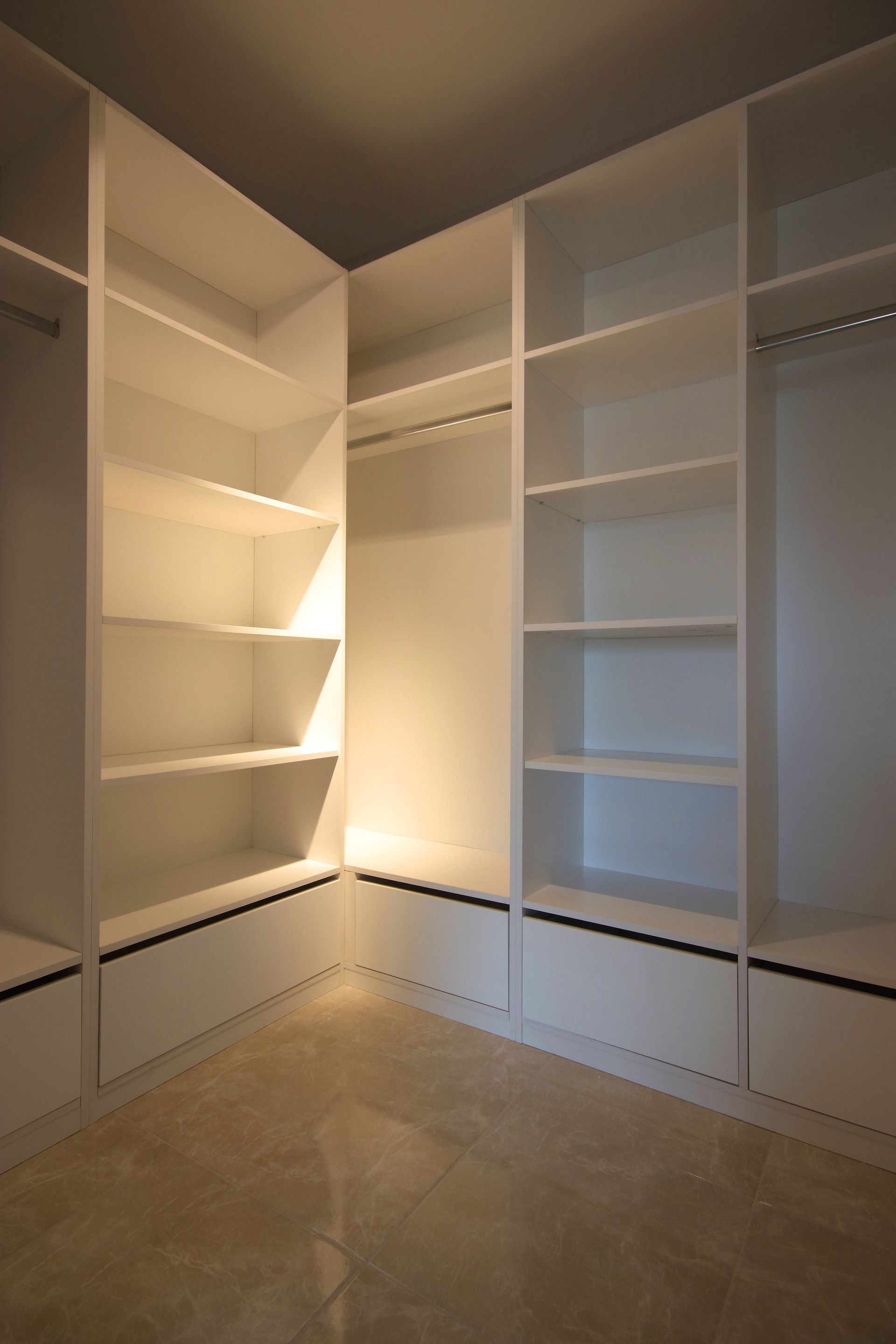 Dressing vide avec étagères encastrées blanches et moquette beige, éclairé par un plafonnier central.