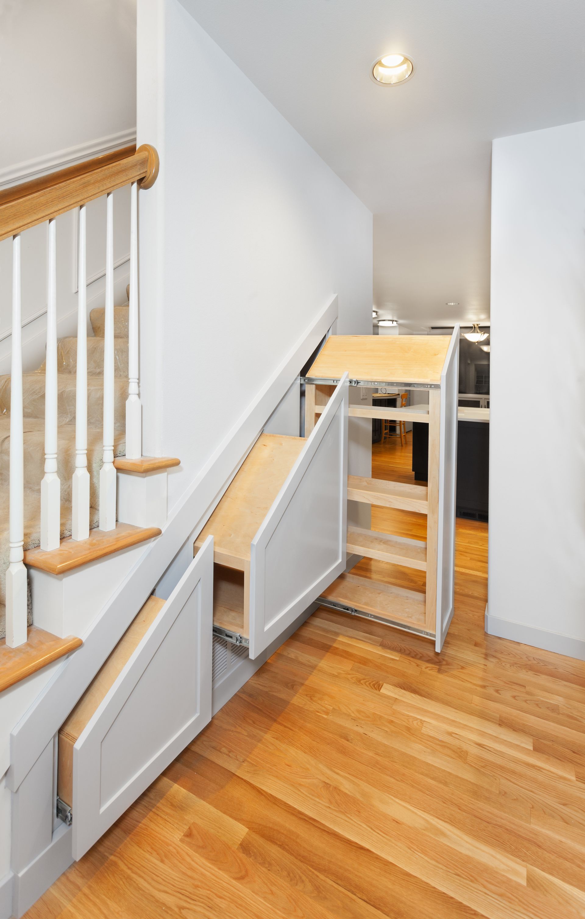 Placard de rangement sous l'escalier dans un couloir avec parquet et murs blancs