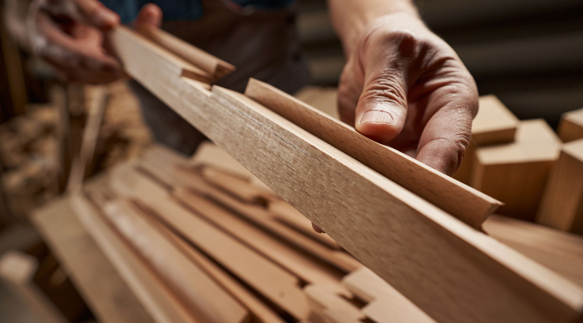 Des mains inspectent des planches de bois empilées dans un atelier de menuiserie