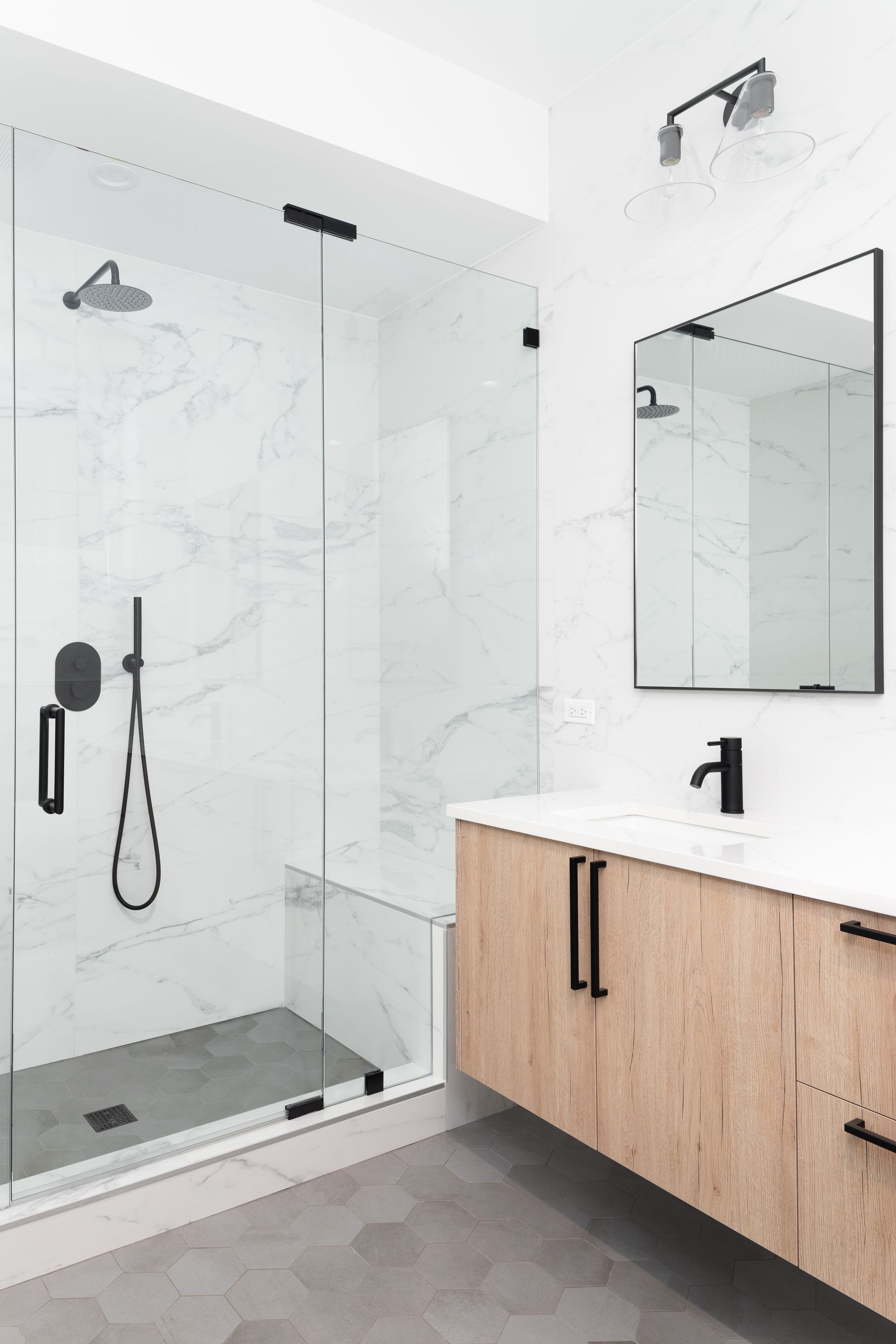 Salle de bains moderne blanche avec douche en verre, robinetterie noire et meuble-lavabo en bois avec miroir.