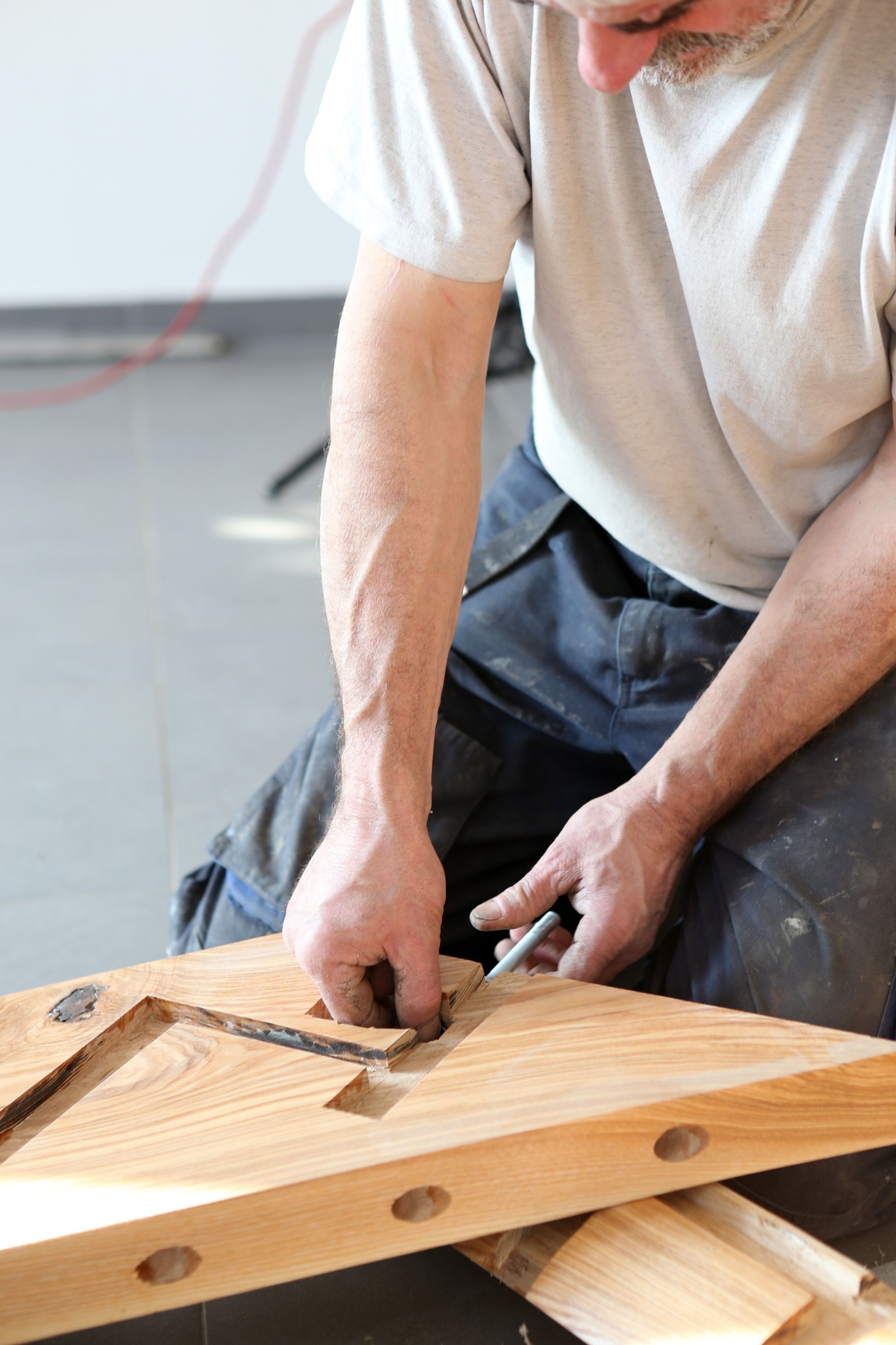 Une personne utilise un ciseau sur une planche de bois dans un atelier, en train de façonner un morceau de bois.