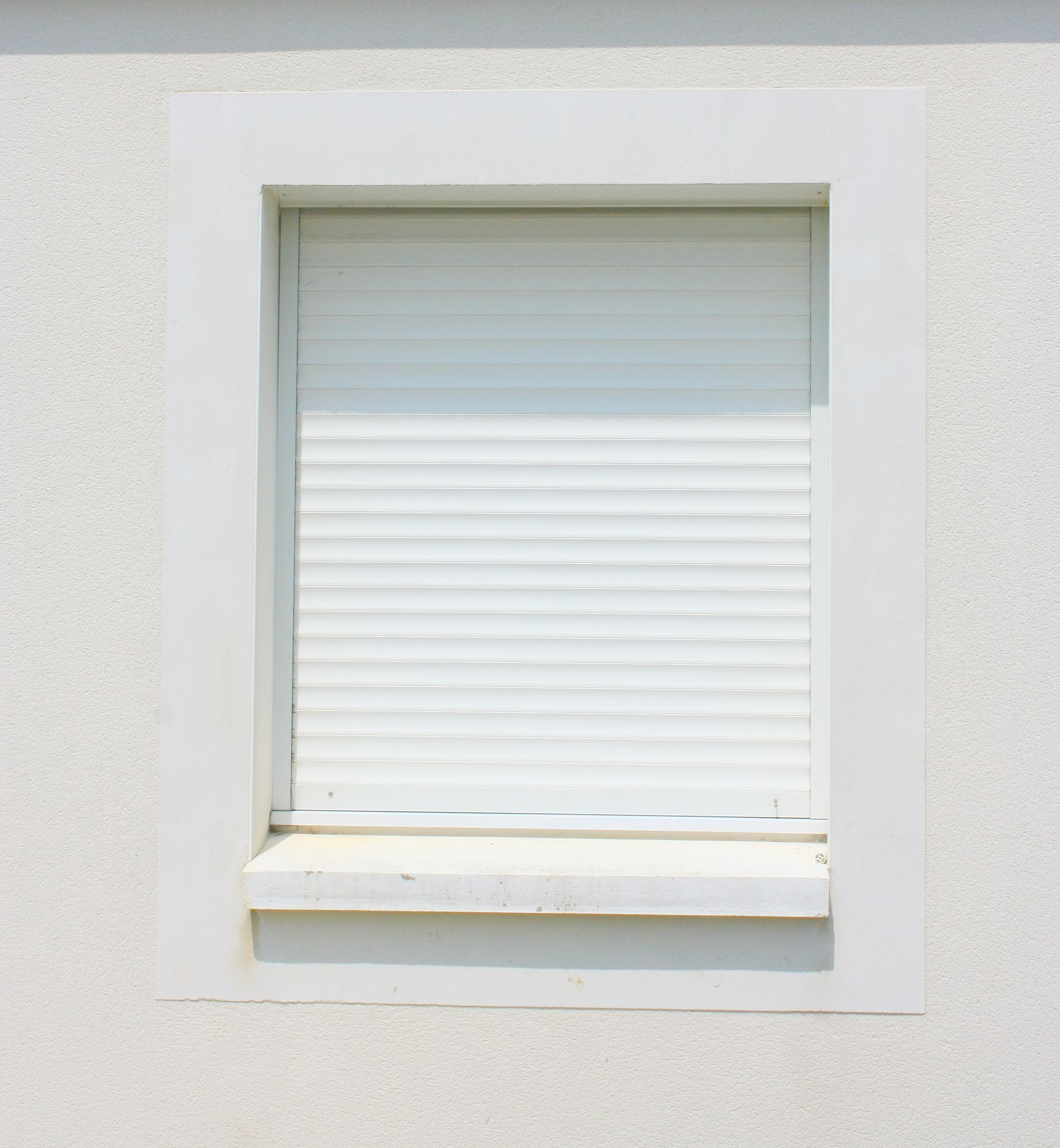 Volet de fenêtre blanc fermé encastré dans un mur en stuc clair.