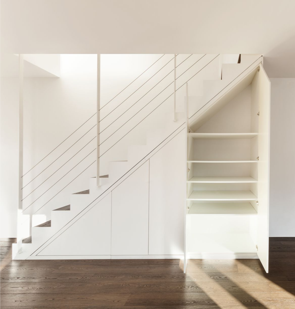 Escalier blanc avec étagères et placards intégrés dans une pièce lumineuse avec parquet foncé.