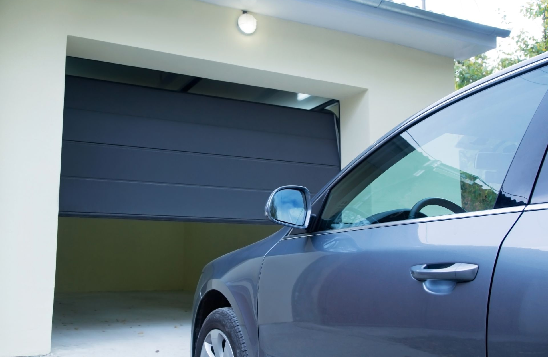 Voiture bleue garée devant un garage ouvert dont la porte est sombre.