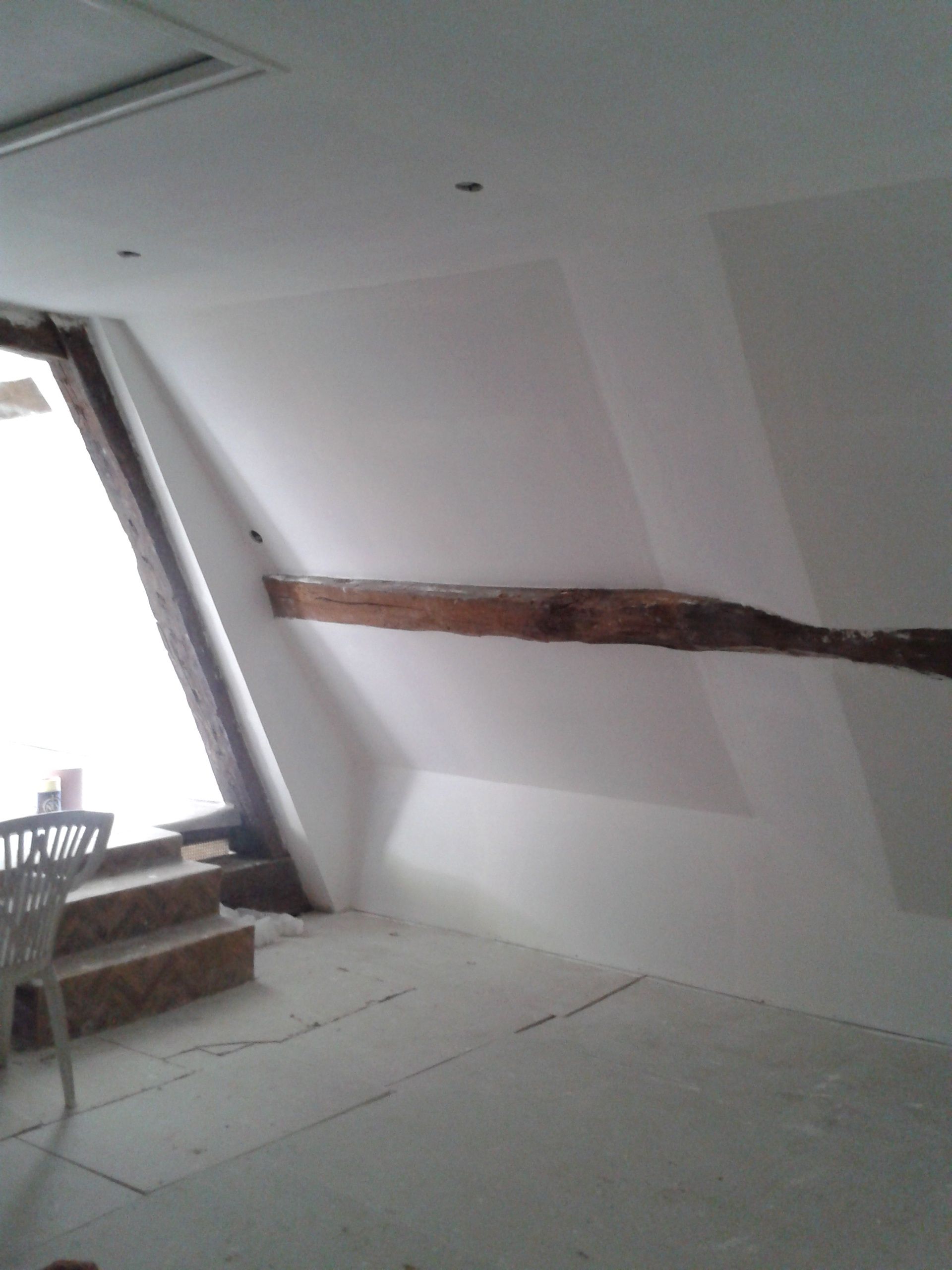 Mur intérieur blanc endommagé, présentant une longue fissure horizontale près d'une fenêtre d'escalier.