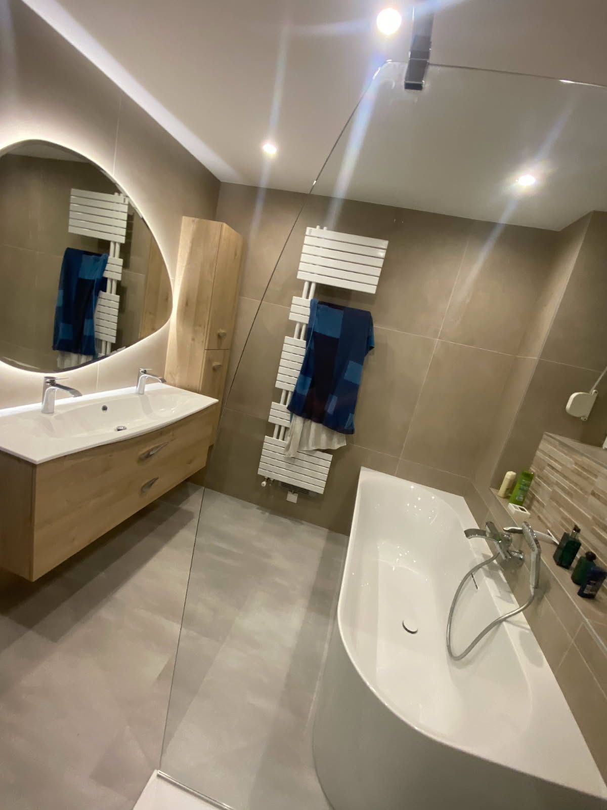 Salle de bains moderne avec baignoire, meuble-lavabo en bois et grand miroir.