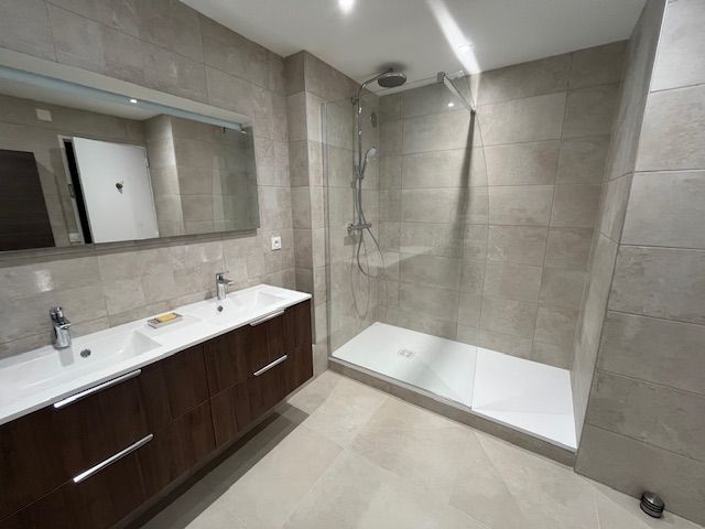 Salle de bains moderne avec douche à l'italienne, meuble-lavabo double vasque, grand miroir et carrelage aux tons neutres.