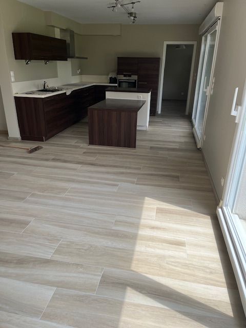 Cuisine moderne avec placards brun foncé, sol clair imitation bois et grande porte coulissante en verre.