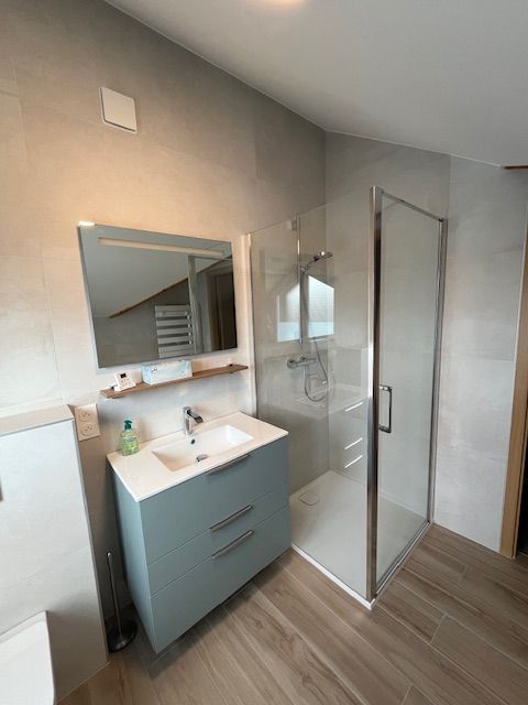 Salle de bains moderne avec meuble-lavabo bleu, douche en verre, miroir et murs aux tons neutres.