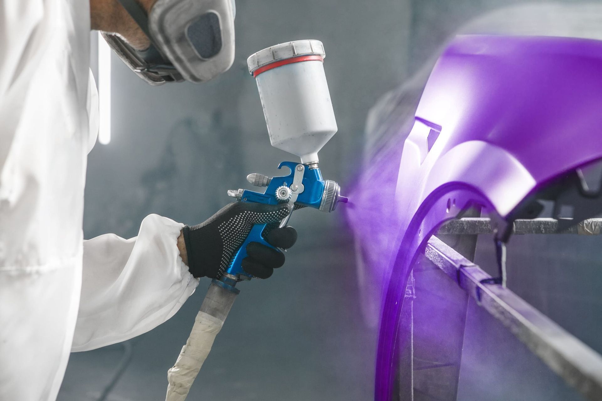 Un técnico pulverizando pintura morada sobre la carrocería de un coche en un taller