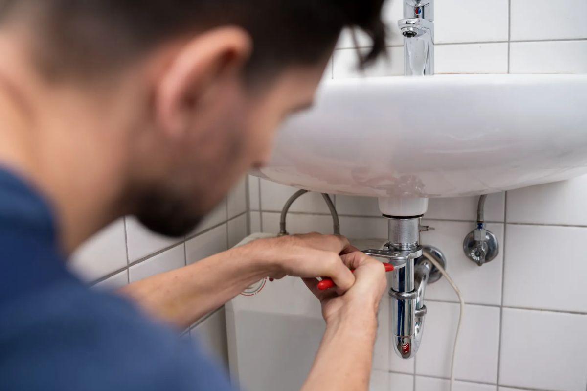 Un hombre está arreglando un lavabo en un baño con un destornillador.