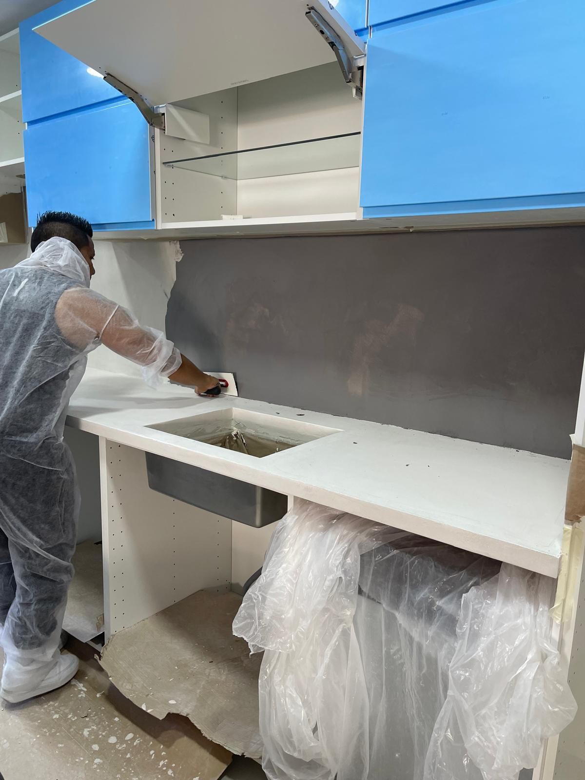 Un hombre está trabajando en una cocina con gabinetes azules y encimeras blancas.