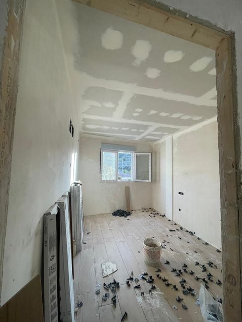 Se está remodelando una habitación con piso de madera y paredes blancas.