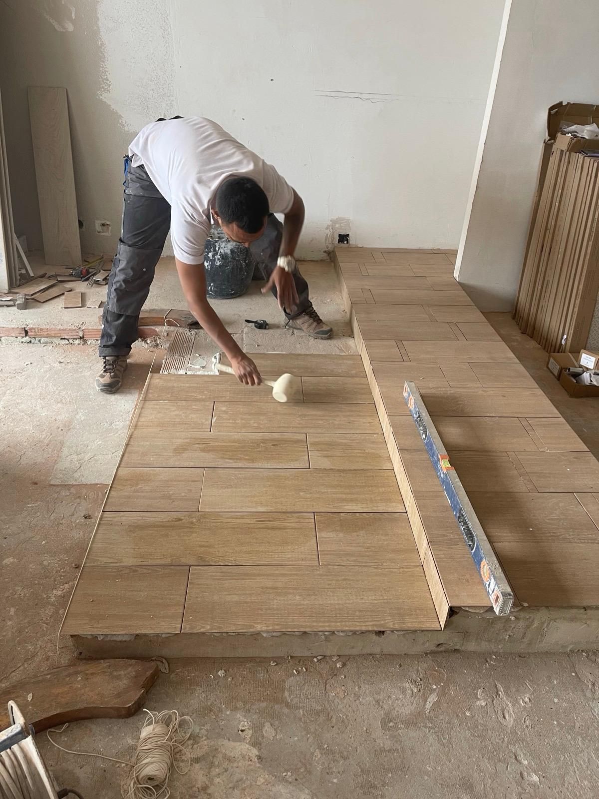 Un hombre está colocando baldosas en un piso de madera en una habitación.